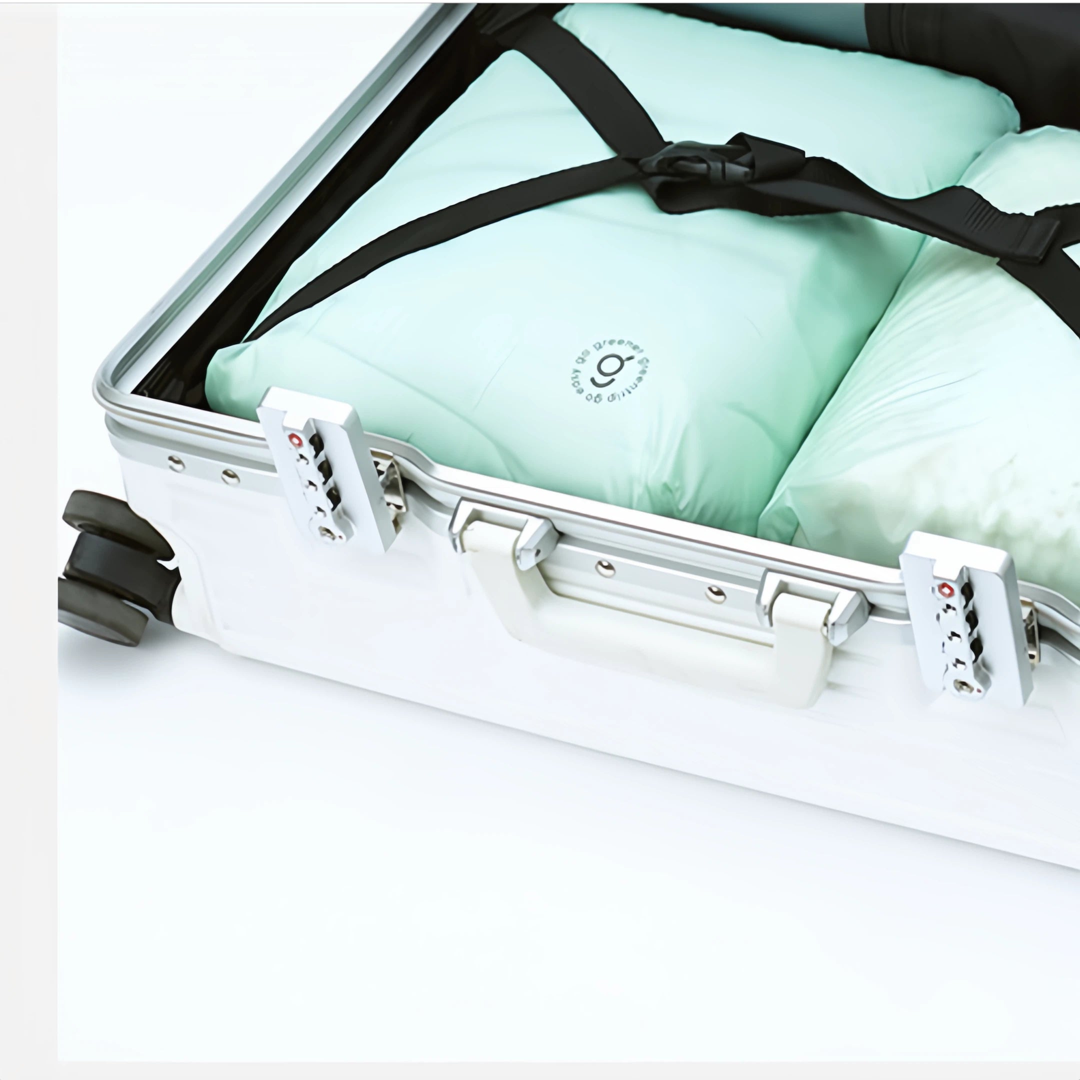 White suitcase with a green garment inside, secured with a black strap.