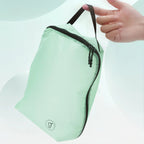 Light green travel pouch with black zipper held by a hand on a light gray background