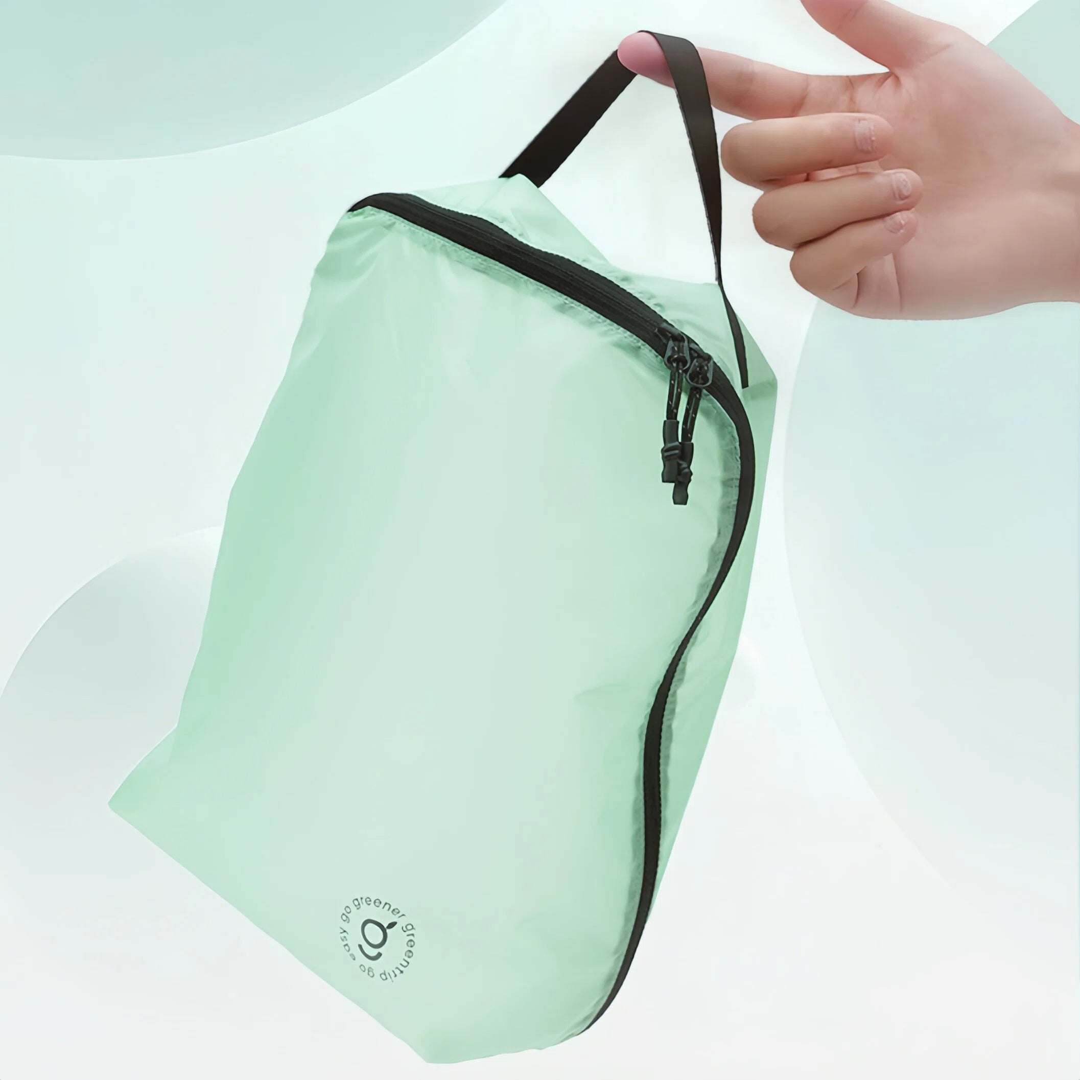 Light green travel pouch with black zipper held by a hand on a light gray background