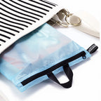 Light blue travel bag with black zipper and strap, attached to a white bag with black stripes.