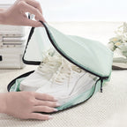 White sneakers being placed into a green travel bag on a light surface.