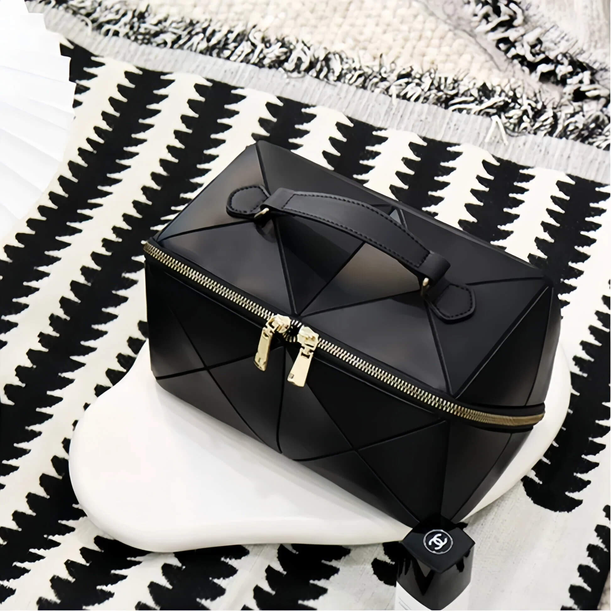 Black geometric makeup bag with gold zipper on a black and white patterned surface