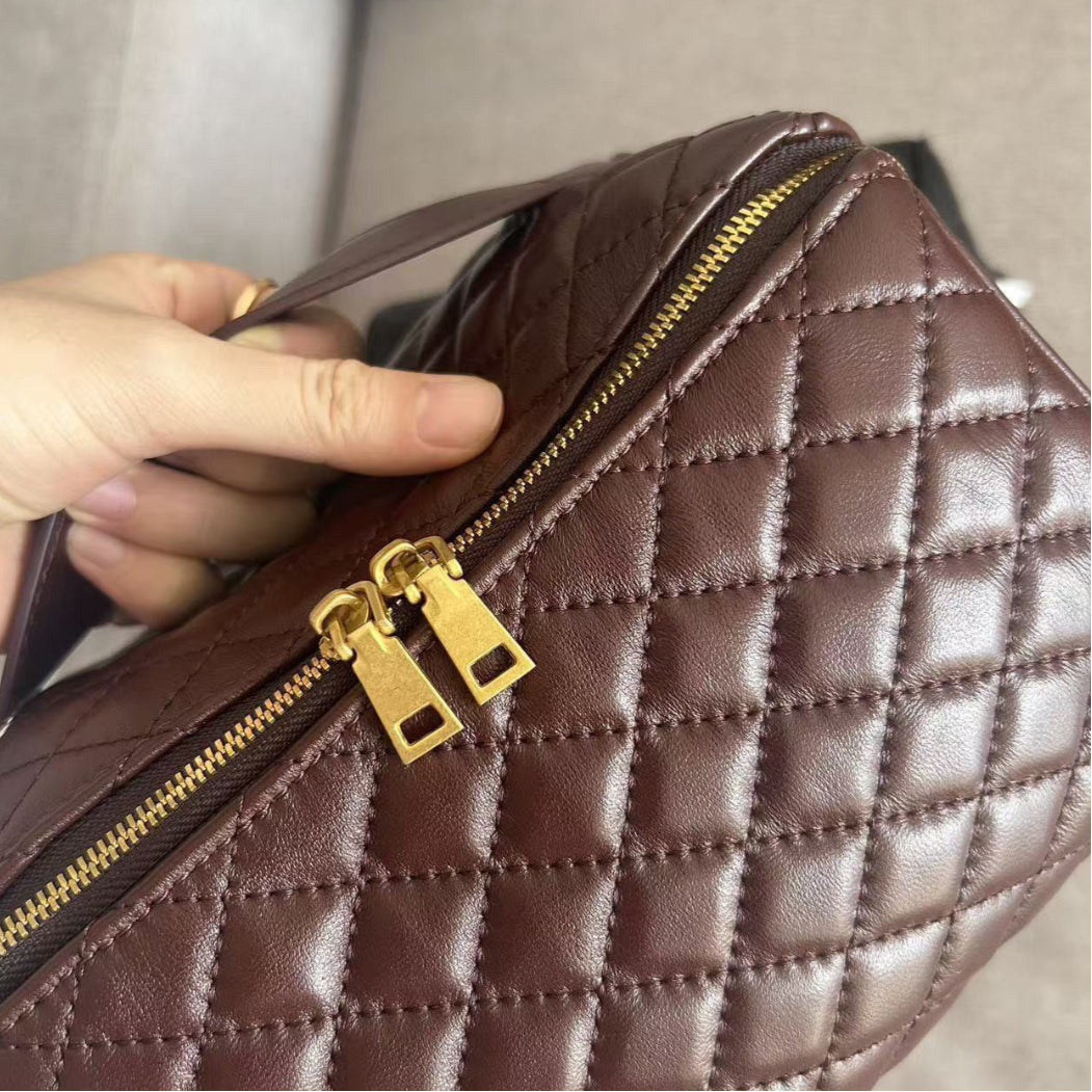 Wine-coloured quilted handbag with gold zipper held by a hand against a neutral background