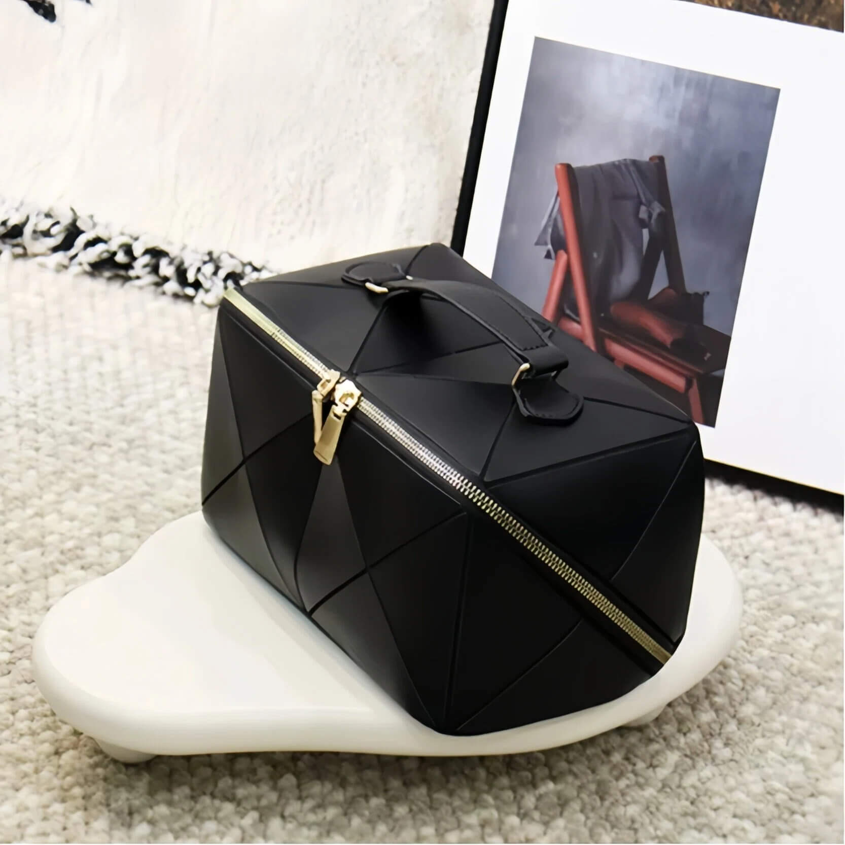 Black geometric makeup bag with gold zipper on a textured surface