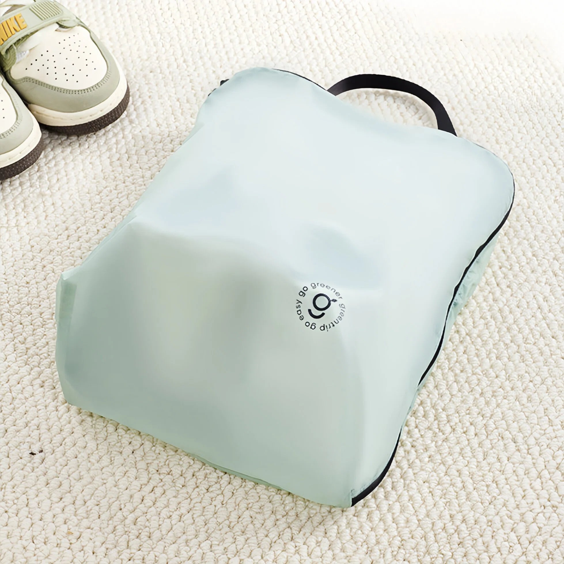 Light green travel bag on a textured surface with shoes in the background