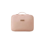 A light pink rectangular zippered travel pouch with a top handle and a small gold-tone brand plaque, shown against a plain white background.