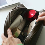 Hand reaching into a leather bag filled with various items including bottles and containers.