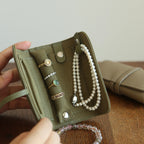 Green jewelry case with rings and a pearl necklace on a wooden surface