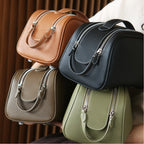 Four leather toiletry bags in brown, black, olive grey, and green against a neutral background.