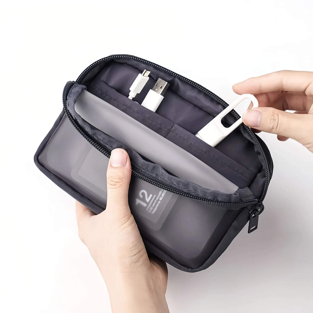 A grey zippered travel organizer pouch held open by two hands, showing its interior compartments with a translucent ID window, a gray sleeve, and white accessories inside, on a clean white background.