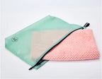 Green travel storage bag with pink textured cloths on a light gray background
