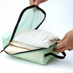 Light green travel bags with white folded fabric held by a hand on a white background