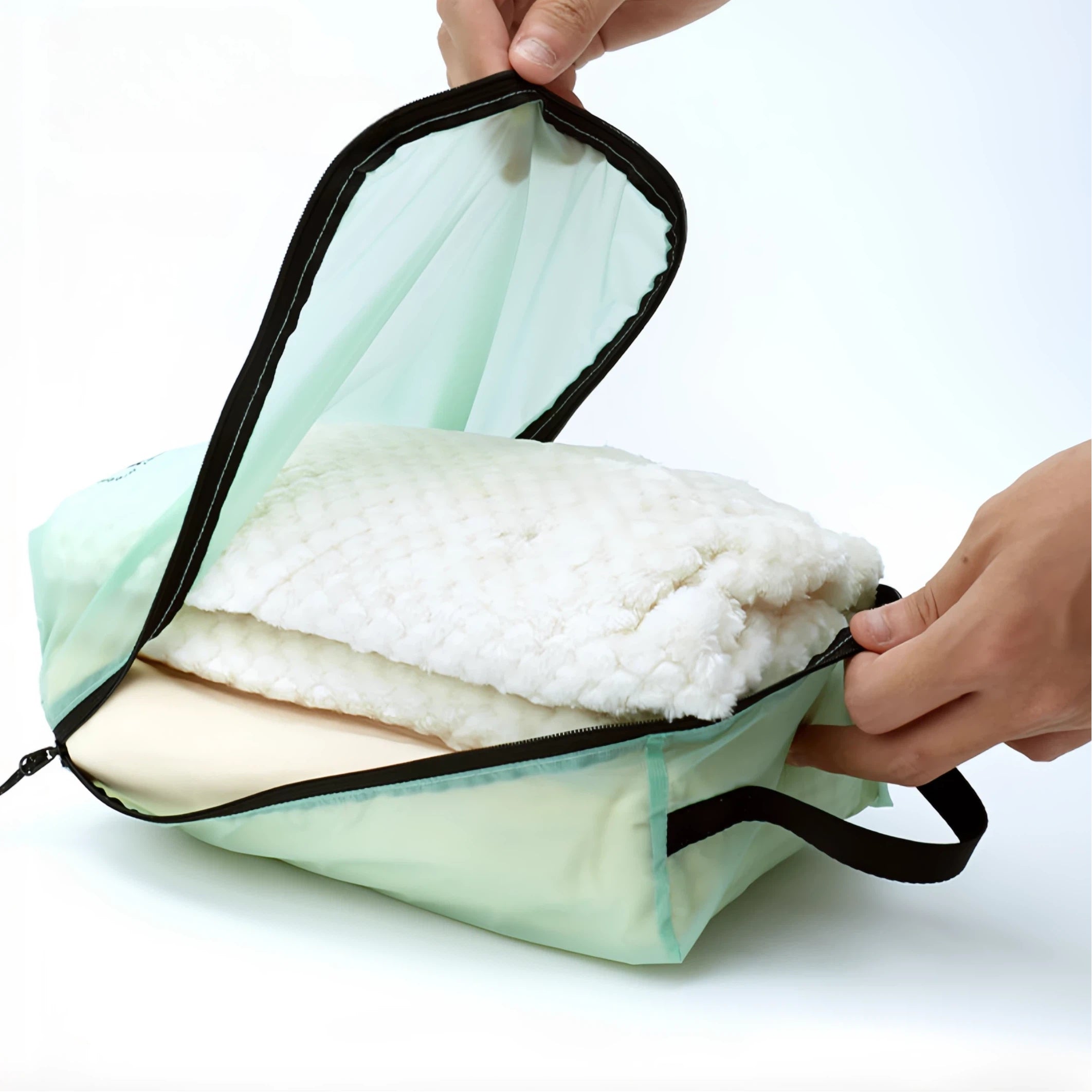 Light green travel bags with white folded fabric held by a hand on a white background