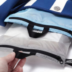 Close-up of grey and blue travel bags and black zipper, held by a hand.