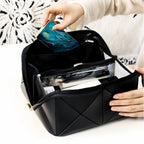 Person opening a black quilted makeup bag to reveal its contents on a white surface.