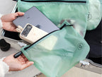 Person holding a green travel storage bag with electronic devices inside, next to an open suitcase.