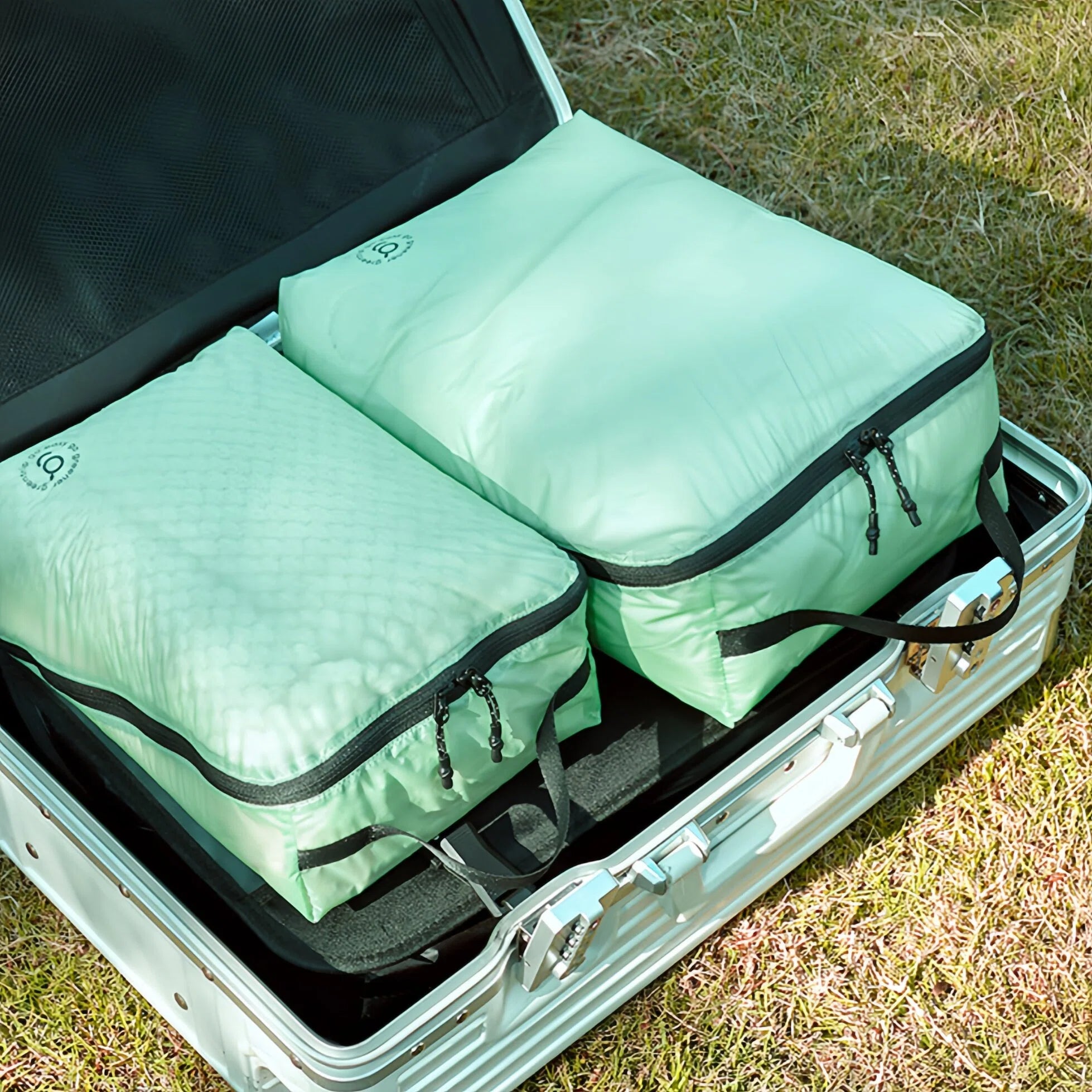 Two green travel bags in an open suitcase on grass