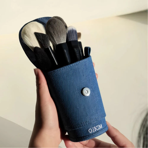 Set of makeup brushes in a denim holder on a light background.
