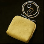 Yellow leather jewellery bag with a pearl necklace and rings on a dark background