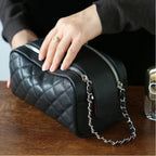 Person holding a black quilted makeup bag with a chain detail on a wooden surface.