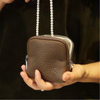 Olive grey leather jewellery bag with pearl chain held by a person against a dark background