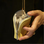 Hand holding a yellow leather jewellery bag with jewelry, against a dark background