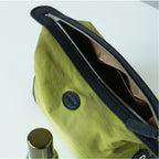 Close-up of a green nylon bag with black trim and a silver zipper, showing the interior lining and a round black brand patch.