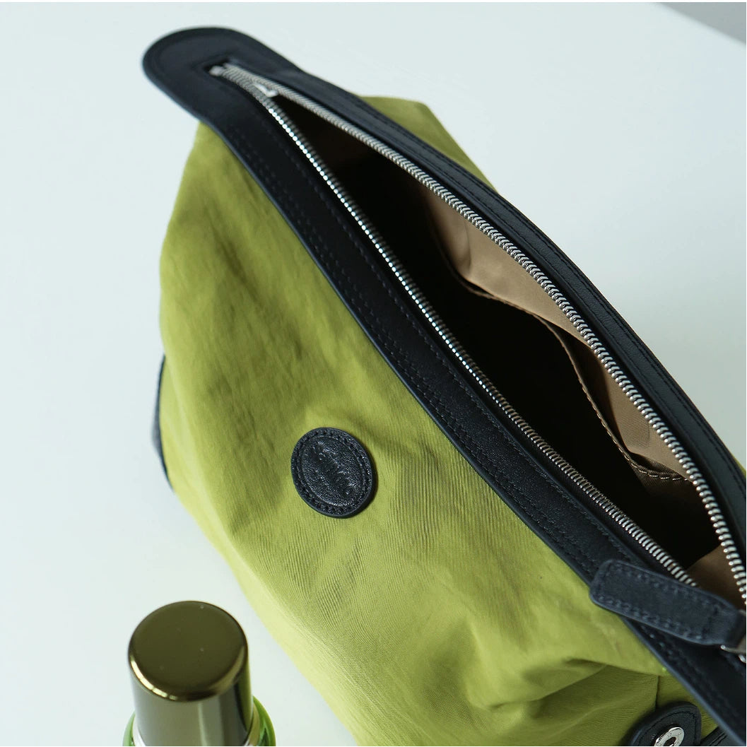 Close-up of a green nylon bag with black trim and a silver zipper, showing the interior lining and a round black brand patch.