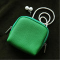 Green leather pouch with a pearl necklace on a dark background