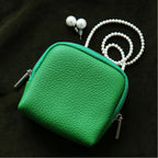 Green leather pouch with a pearl necklace on a dark background