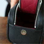 Black leather makeup bag with a silver zipper and button on a wooden surface