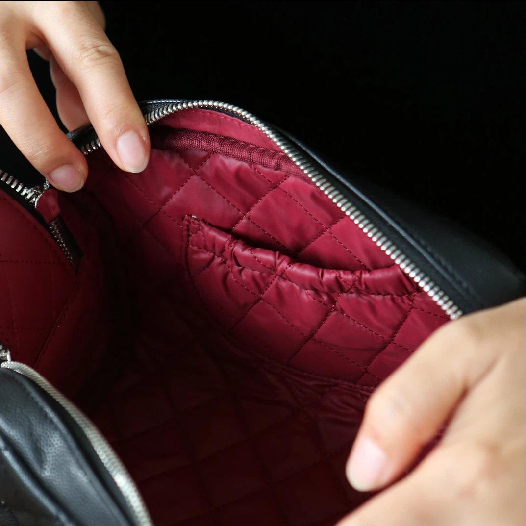 Close-up of a person opening a black quilted makeup bag.