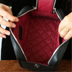 Person opening a black leather makeup bag with a red quilted interior.