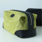 A green nylon cosmetic pouch with black leather trim and a silver zipper, shown on a light gray background with a second black pouch partially visible in the background.