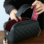 Black quilted makeup bag with a red interior, held open by a hand on a wooden surface.