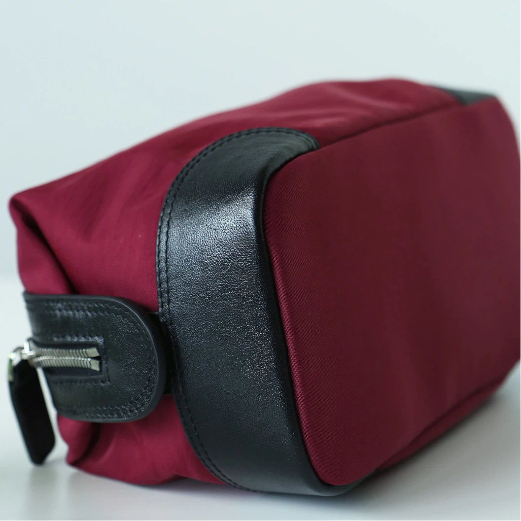 A burgundy nylon cosmetic pouch with black leather trim and a black zipper pull, shown on a light gray background.