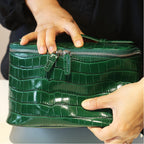 A close-up of a person holding a glossy green zippered pouch or cosmetic case with both hands.