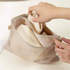 Person holding a beige mesh bag with clothes inside on a light background