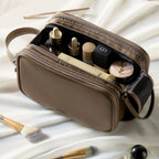Olive grey dual-zip cosmetic bag with makeup products and brushes on a light background