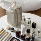 Beige dual-zip cosmetic bag with skincare products and makeup tools on a white surface
