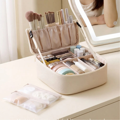 A beige makeup organizer case sits open on a light vanity table, filled with cosmetics and brushes. A matching translucent pouch lies in front, and part of a lit mirror reflecting the model's arm is visible in the background.