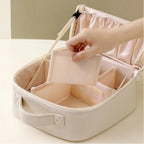 A light beige cosmetic organizer case with a soft pink satin interior, shown open with a hand placing a matching pink compartment insert inside.