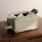 Beige dual-zip toiletry bag with a handle on a wooden surface