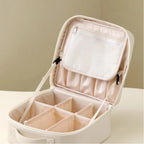 An open cream-colored cosmetic organizer case with multiple interior compartments, a zippered pocket on the inside lid, and a shoulder strap, shown on a plain light background.