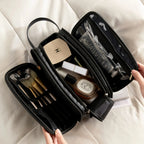 Black dual-zip toiletry bag with various cosmetic items on a light background