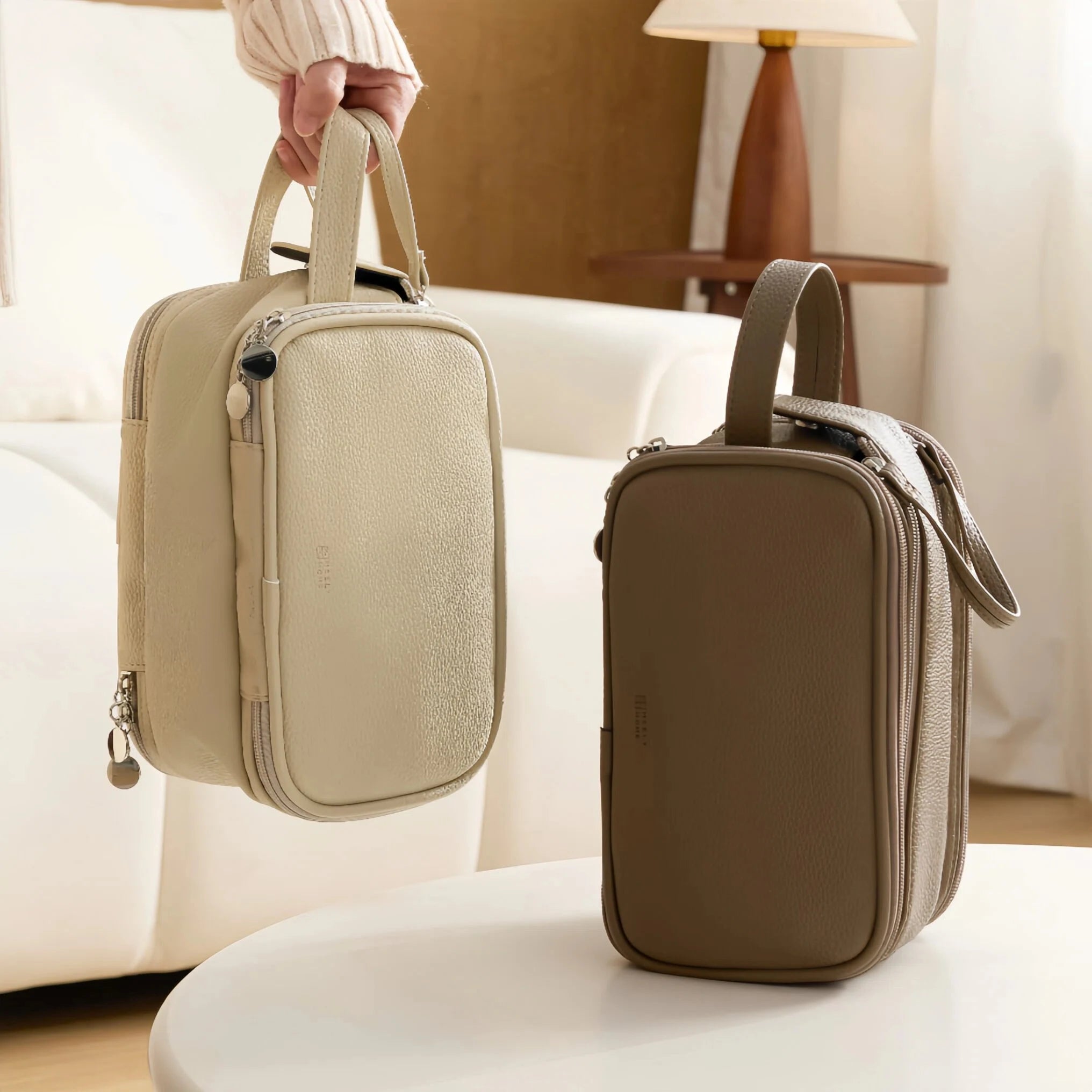 Two dual-zip cosmetic bags on a white surface with a blurred indoor background